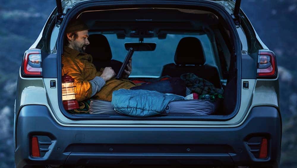 Man relaxing with a laptop in the open cargo area of a Subaru Outback