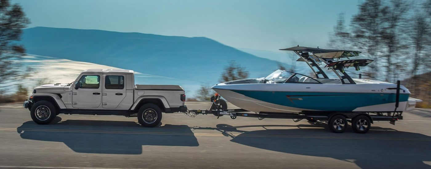 A silver 2023 Jeep Gladiator is towing a boat on an open road.