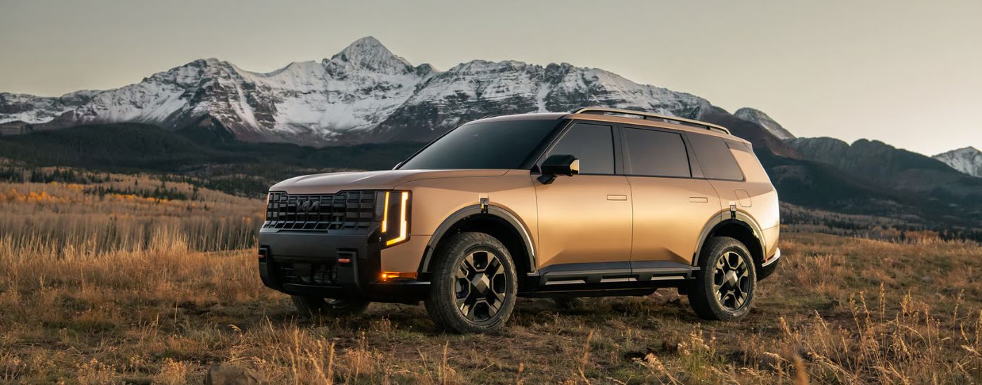 Brown 2027 Kia Telluride X-Pro parked in a field by a mountain.