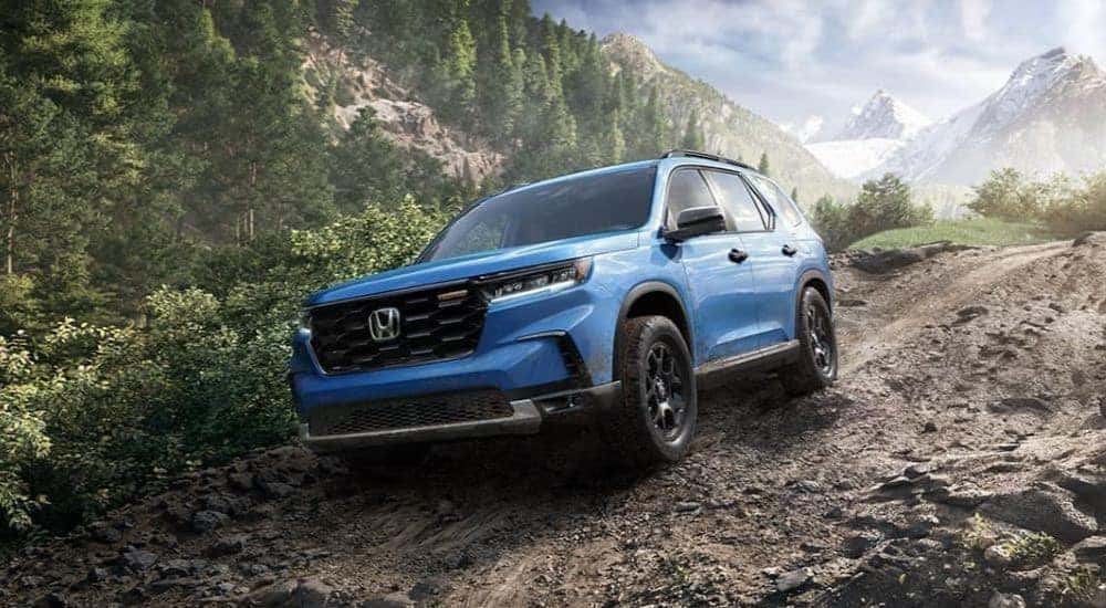 A blue 2023 Honda Pilot Trailsport is shown driving off-road.