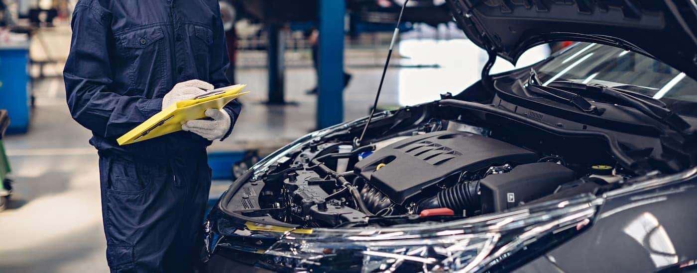 "A mechanic is holding a yellow clipboard next to a car.