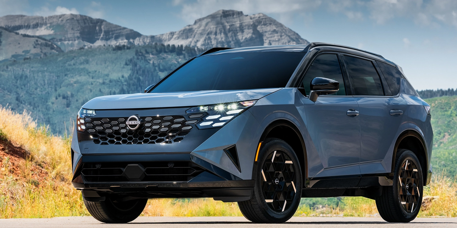 Gray Nissan Rogue Rock Creek SUV with a black roof and bronze-accented wheels parked on a road with rugged mountains in the background, shown from a front three-quarter angle.