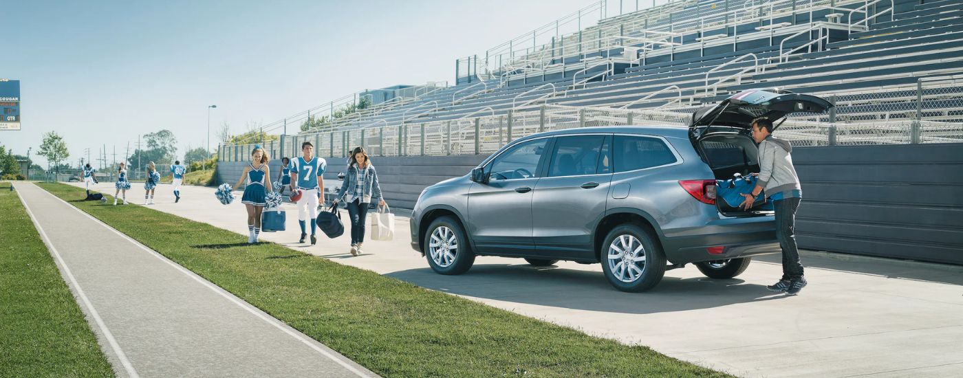 A family is shown getting gear out of a grey 2020 Honda Pilot LX parked at a sports event.