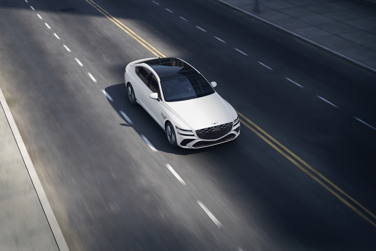 3/4 front passenger overhead view of Genesis G80 in white driving on two lane road