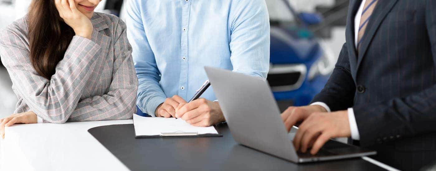 A salesman is on a laptop next to a couple looking at paperwork.