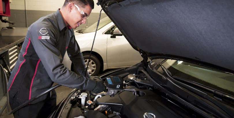 Mechanic in a United Nissan service uniform checking the engine of a Nissan with the hood open
