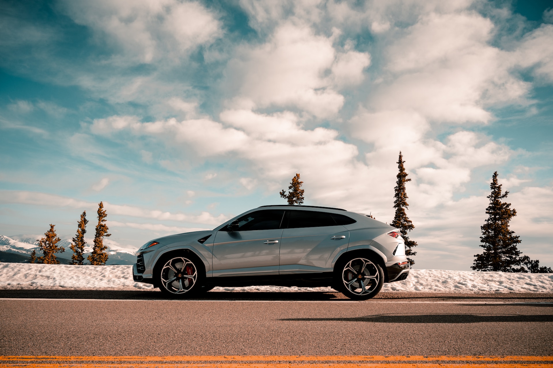 Silver SUV parked on side of road in snow under clouds. 