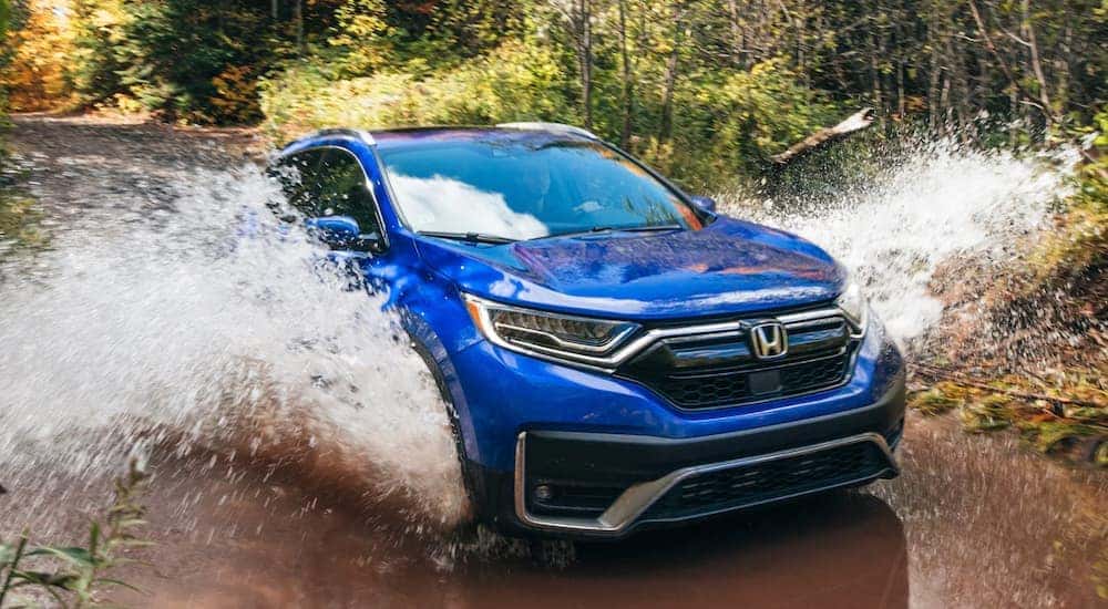 A blue 2021 Honda CR-V Touring is shown off-roading through a puddle.