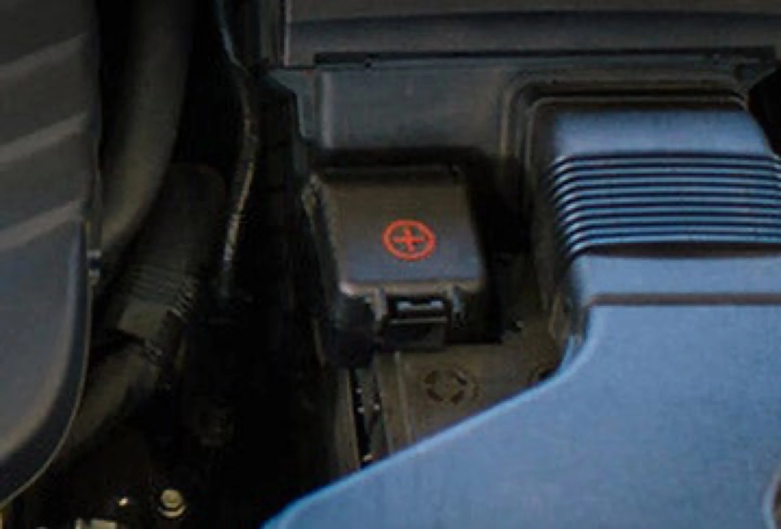 Close-up of a battery's positive terminal cover, which helps prevent corrosion, inside a vehicle's engine bay near the air intake.