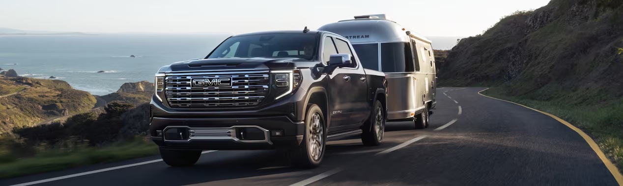 black 2023 GMC Sierra towing an airstream camper on a mountain road