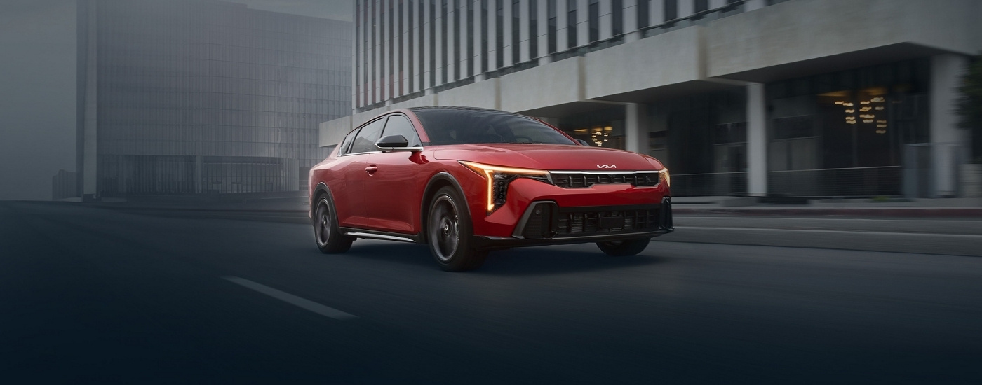 Red 2025 Kia K4 driving to a Kia dealer near St. Cloud