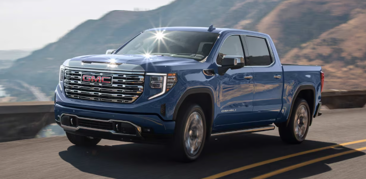 2025 GMC Denali in black paint driving along a coastal highway.