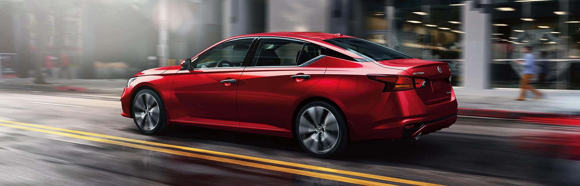 Red Nissan Altima sedan driving on a city street