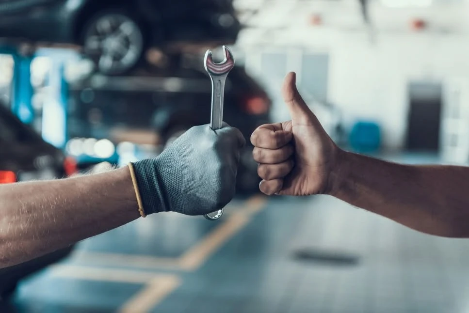 Technician holding a wrench receives a thumbs up from a customer in the service bay, representing satisfaction with Kia service savings