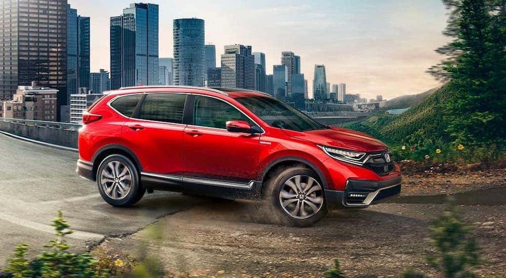 A red 2020 Honda CR-V Hybrid Touring from a Honda dealer near you is driving from a city onto a dirt road.