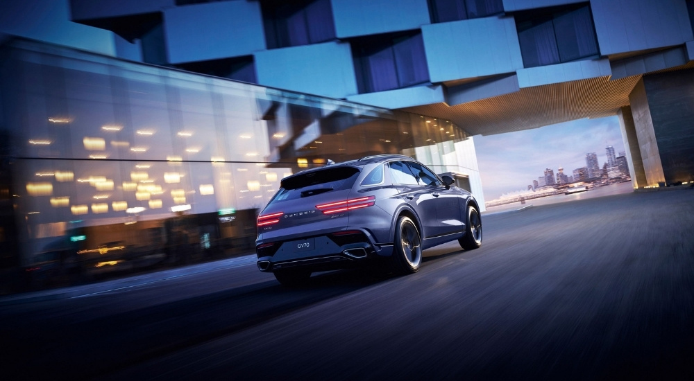 Silver 2026 2026 Genesis GV70 driving past a modern building