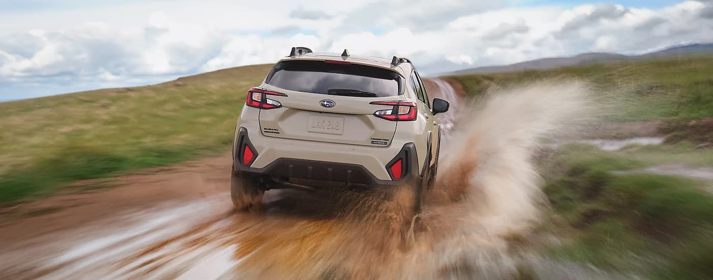 Rear of a white 2026 Subaru Crosstrek Hybrid driving on a muddy road.