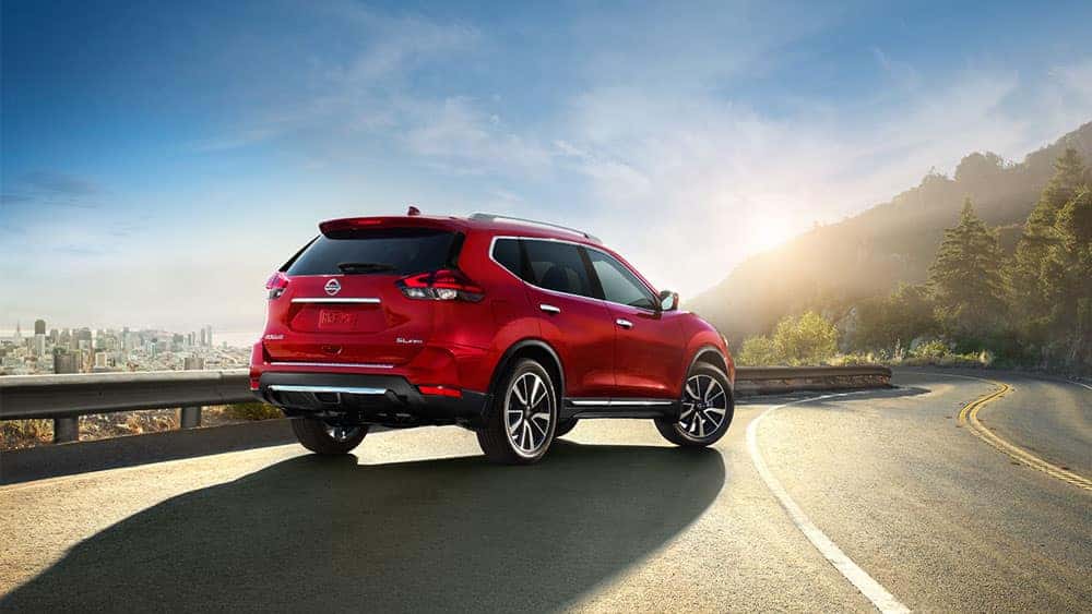 Red 2017 Nissan Rogue on a mountain highway at sunrise, rear view