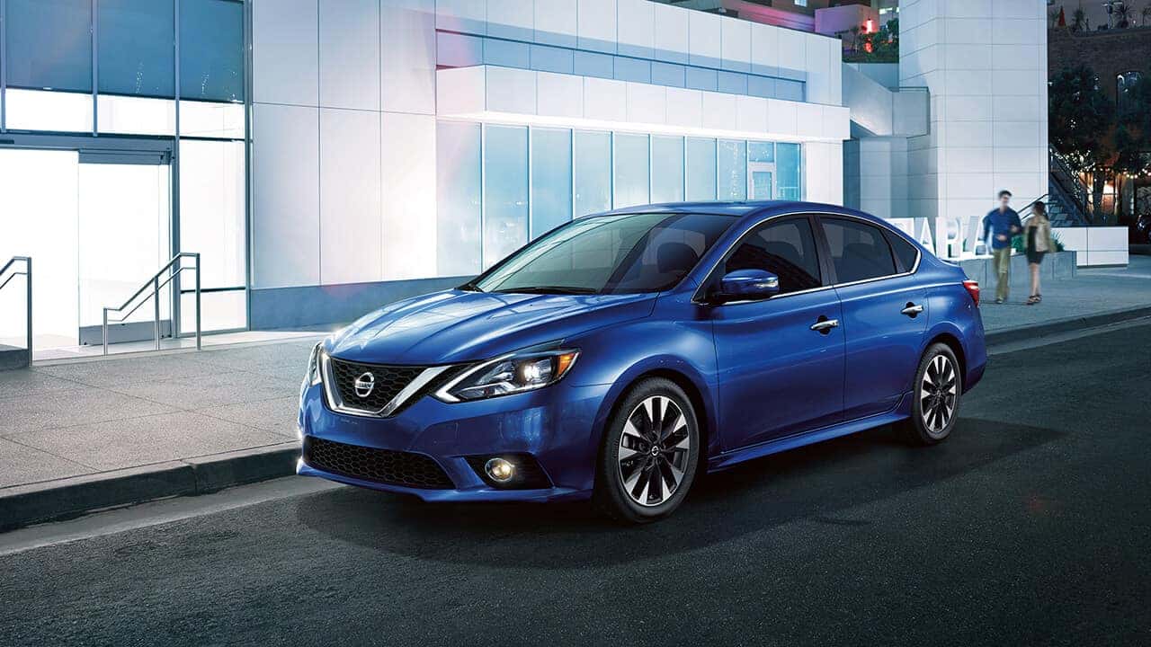 Blue 2017 Nissan Sentra sedan parked in front of a modern glass building