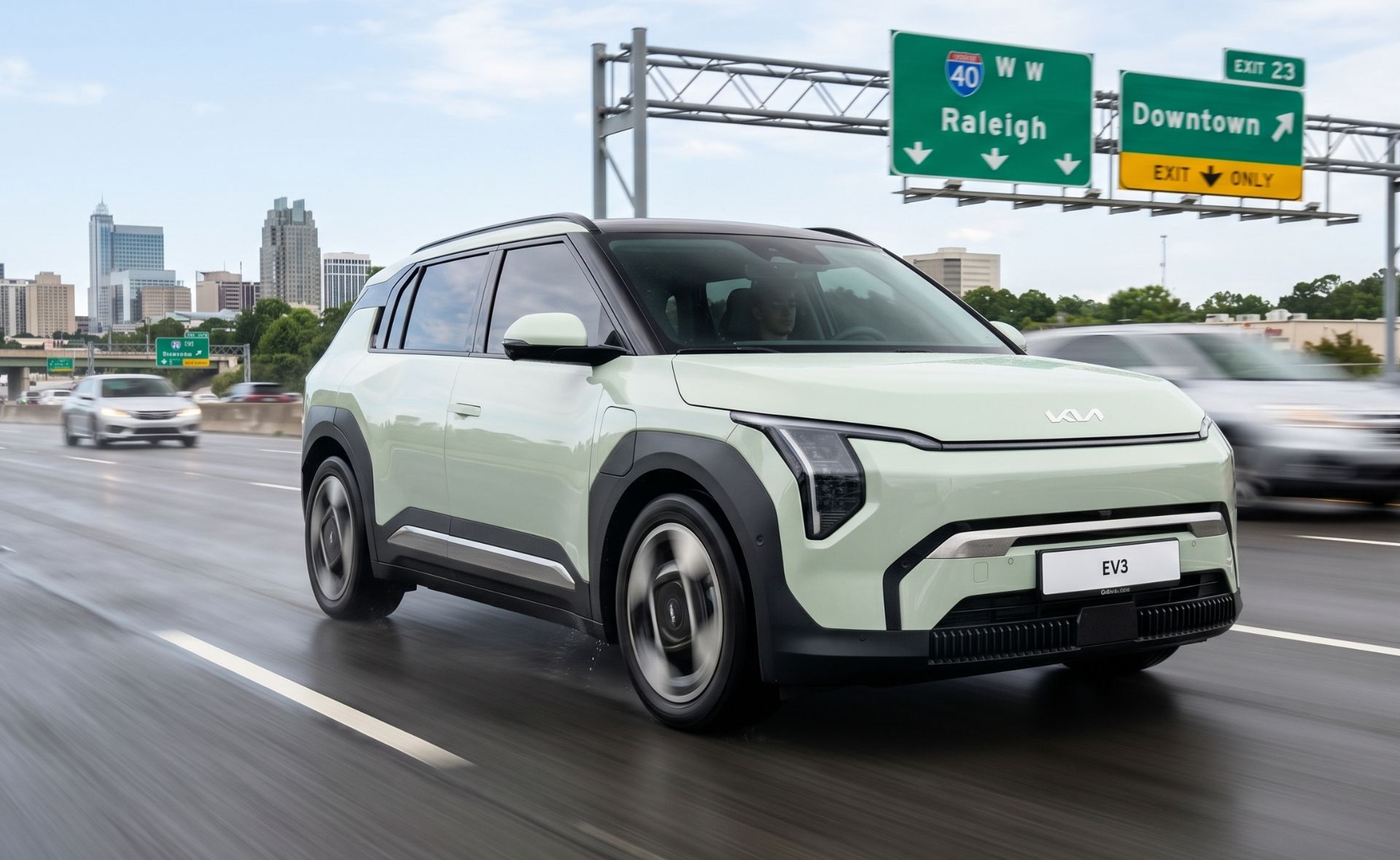A light green Kia EV3 compact electric SUV driving on a highway with the Raleigh city skyline and Interstate 40 highway signs in the background.