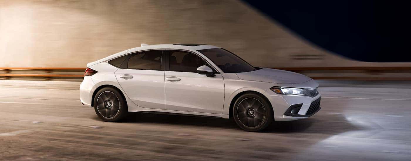 A white 2024 Honda Civic Hatchback Sport Touring driving at night.