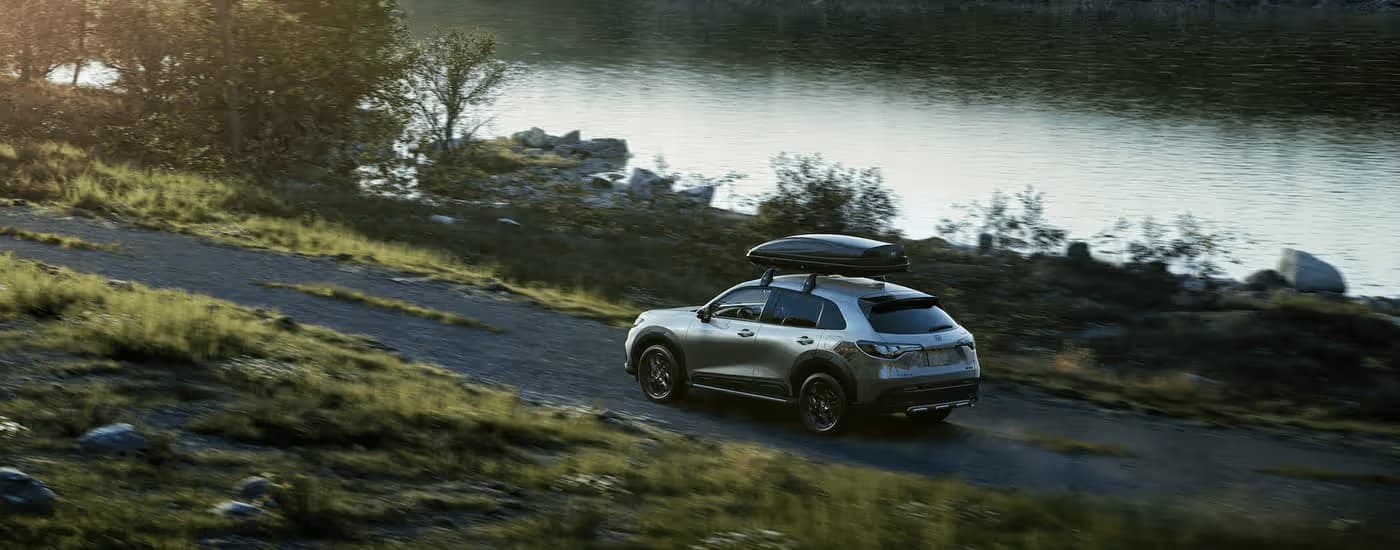 A silver 2023 Honda HR-V is shown from a rear angle driving next to a lake.