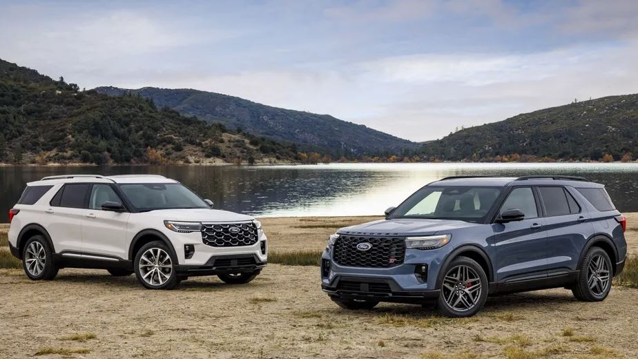 New Ford Explorer 2025 pictured on a beach with mountains in the background; One white model, one gray model.