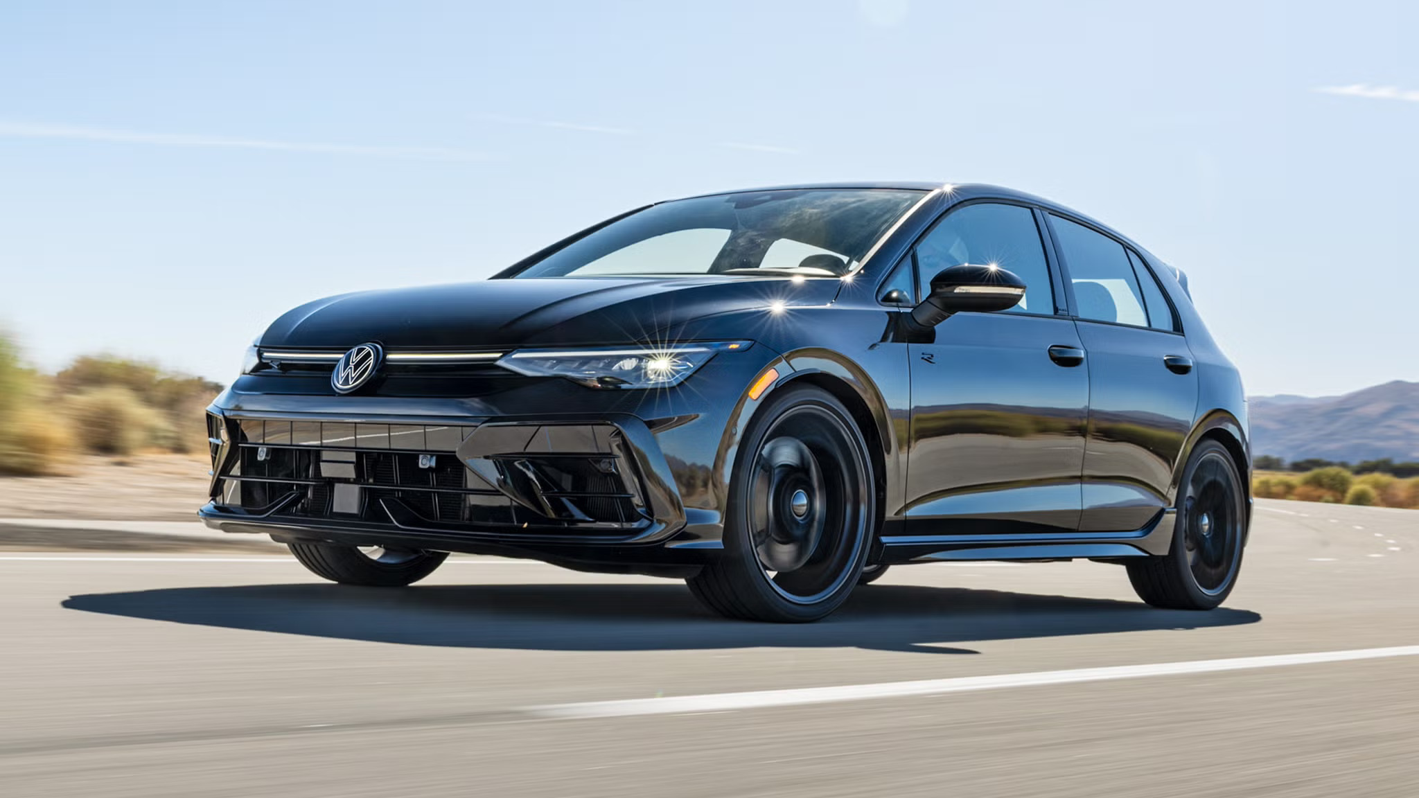 2027 Volkswagen Golf R Black Edition in black driving on a highway, front three-quarter view