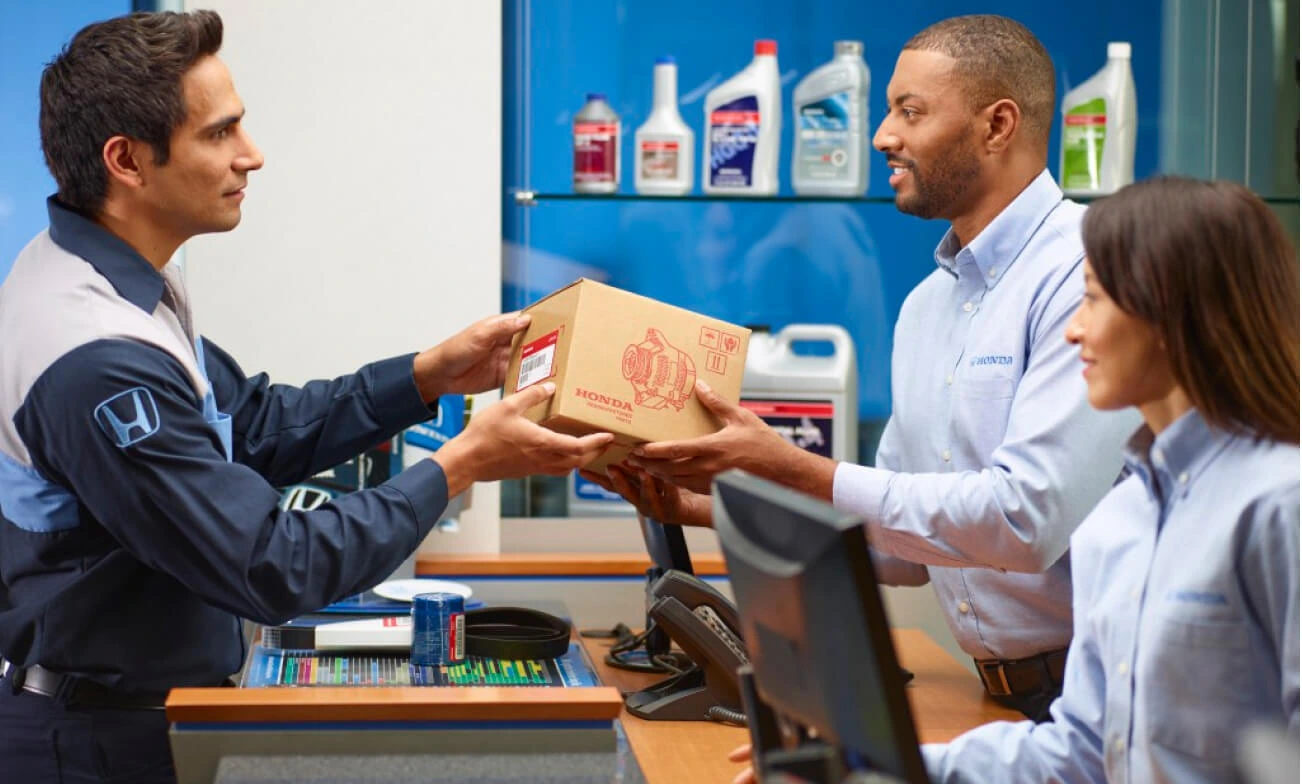 Honda technician hands a genuine parts box to dealership service staff at the parts counter.