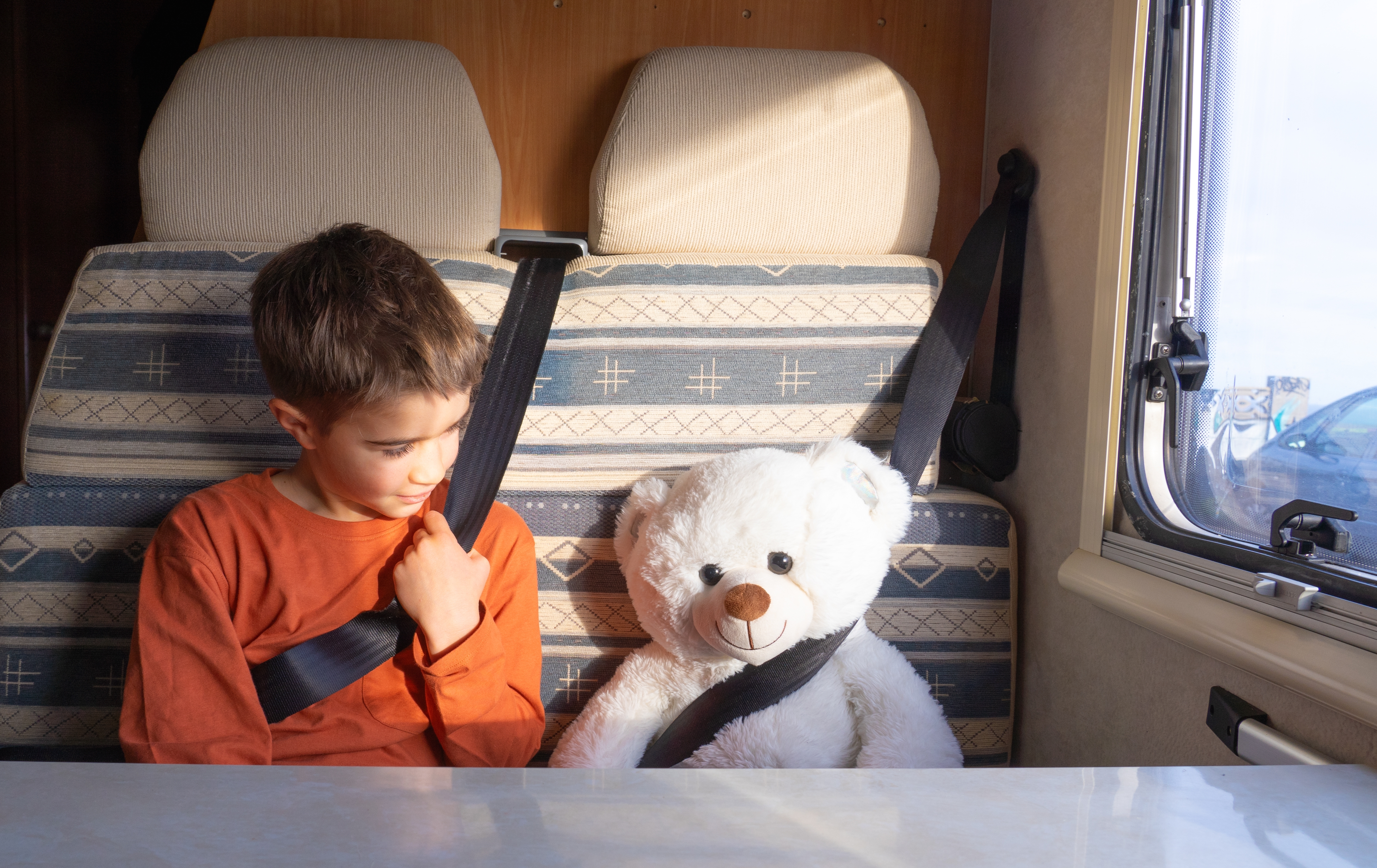 boy and his teddy bear wearing seatbelts in a RV