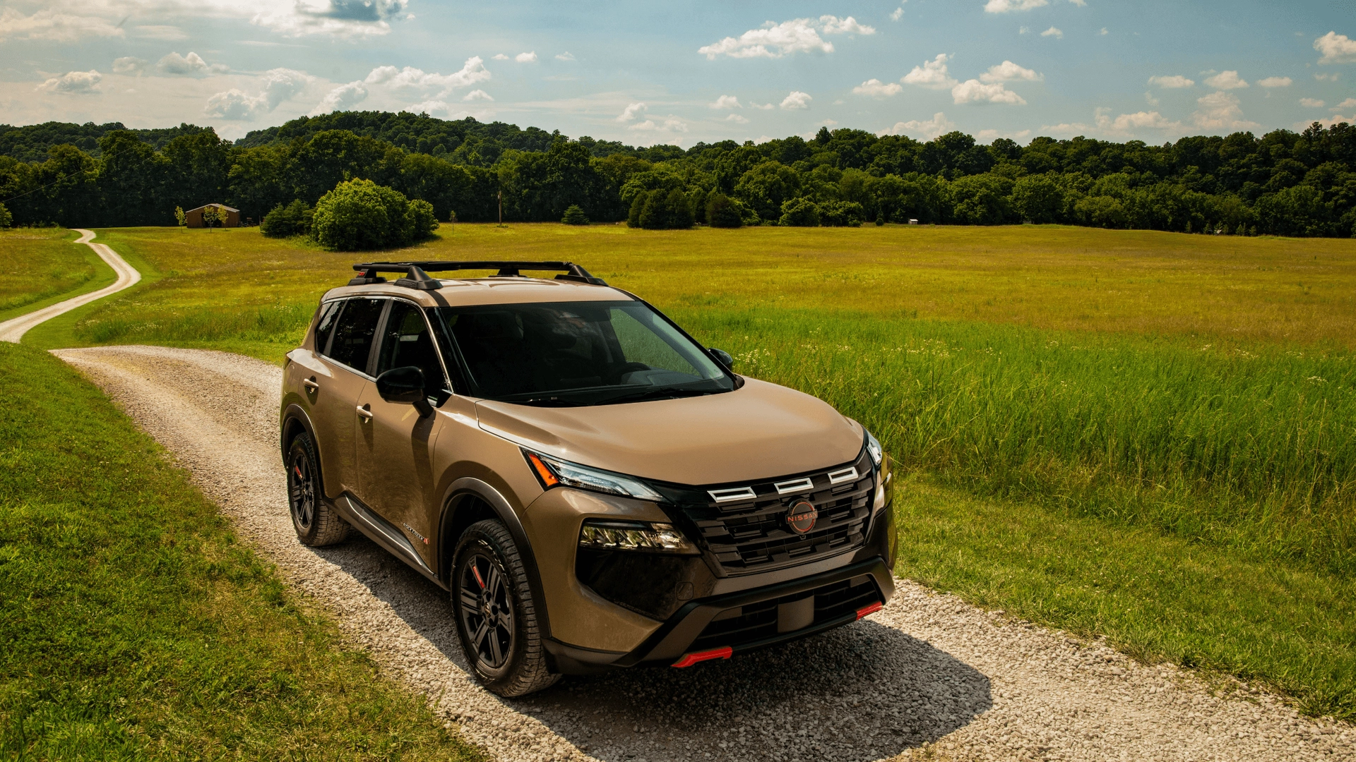 2026 Nissan Rogue® tan SUV driving on gravel road through green fields and wooded hills in daylight