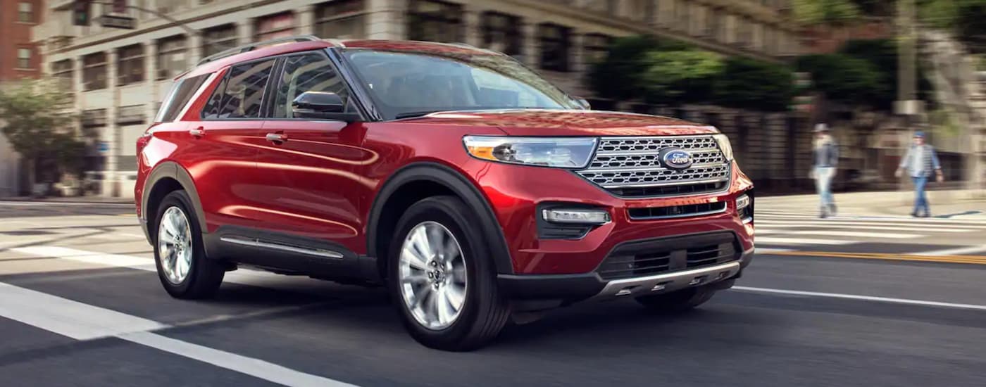 A red 2020 Ford Explorer driving on a city street through an intersection.