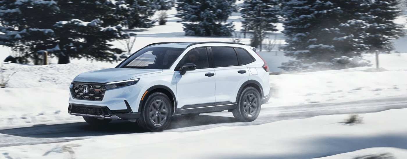 White 2026 Honda CR-V Hybrid TrailSport driving on a snowy trail