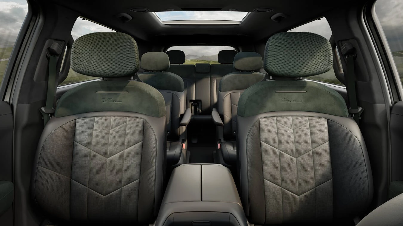 Second-row captain's chairs in a 2027 Kia Telluride HEV X-Line, viewed from behind showing olive suede-and-perforated-leather seatbacks with an embroidered "X-Line" logo, individual armrests, and a center console, beneath an open panoramic sunroof.