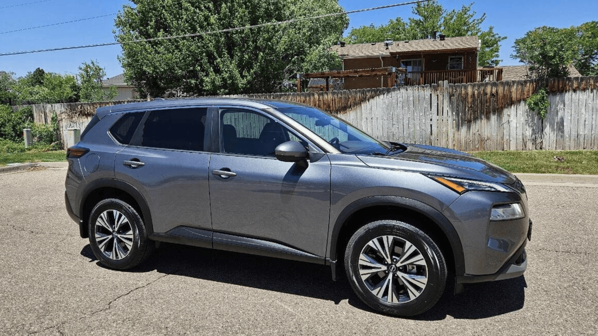 Gray Nissan Rogue® SUV parked on a sunny residential street in front three-quarter view with trees nearby.