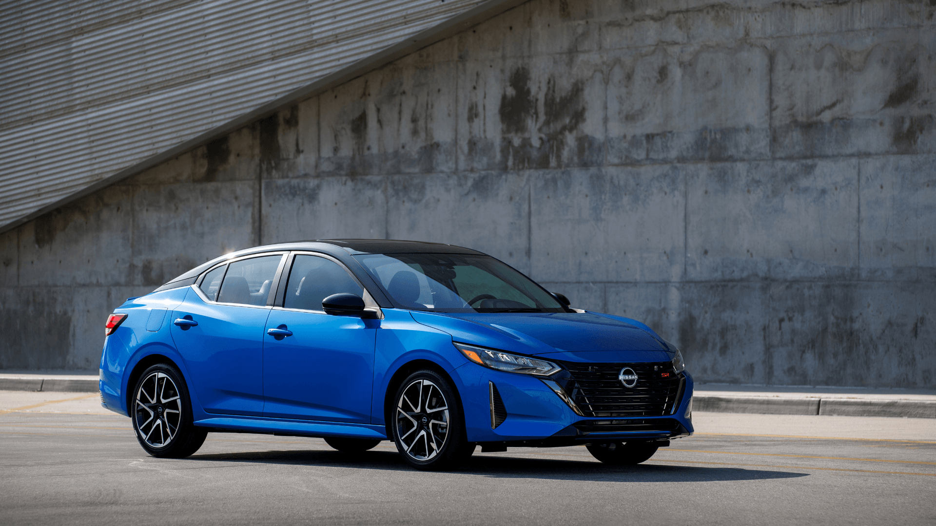 2025 Nissan Sentra® blue sedan parked in front three-quarter view beside a modern concrete building.