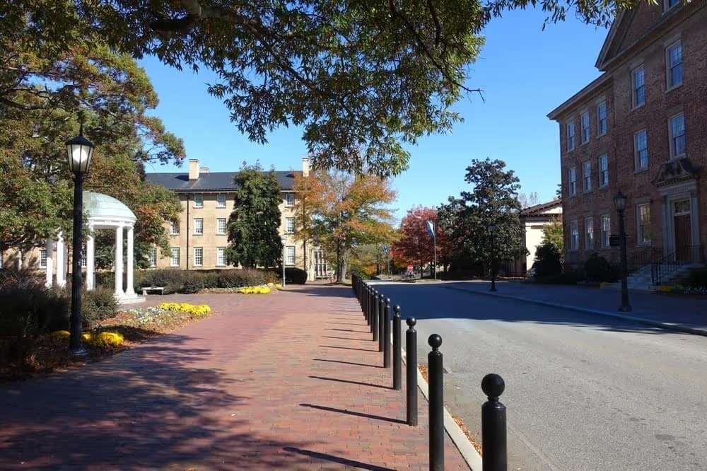 Tree-lined brick walkway past historic campus buildings in Chapel Hill