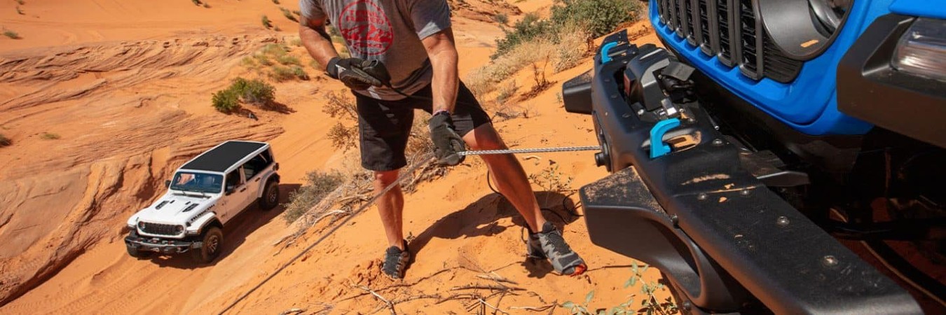 2025 Jeep Wrangler in Distance with Man hitching Tow Cable to Another Close Up Wrangler