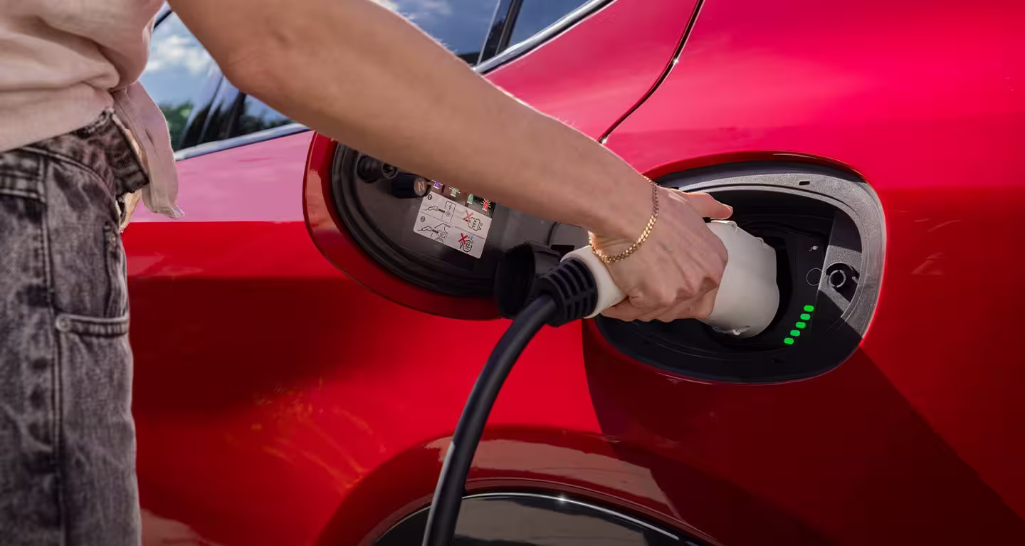 A red car getting charged by someone.