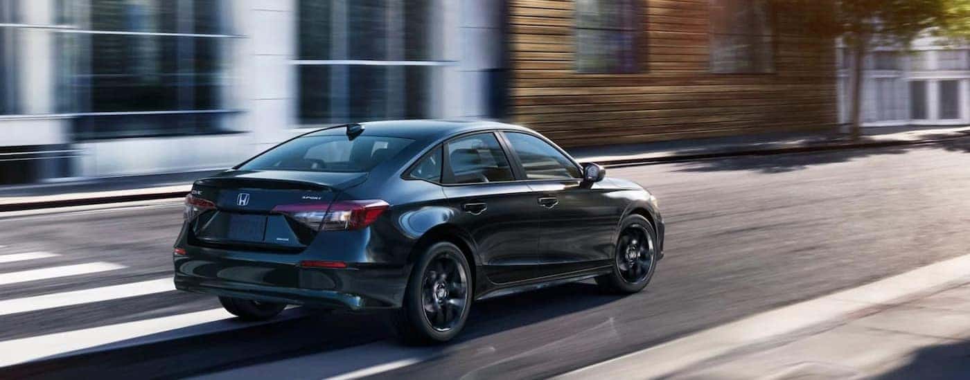 A black 2025 Honda Civic Sport Hybrid is shown driving on a city street.