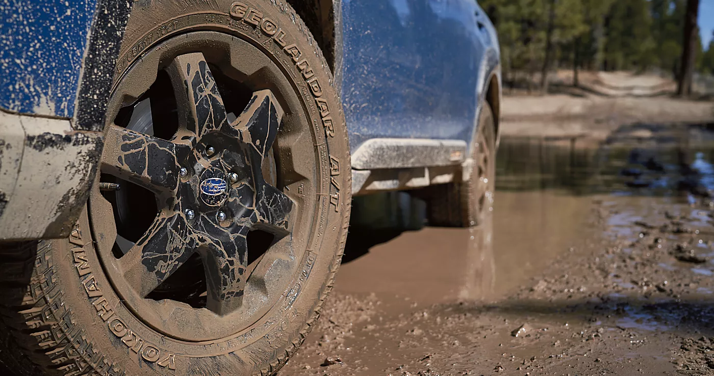 Mud-covered Subaru wheel and tire on a wet dirt trail