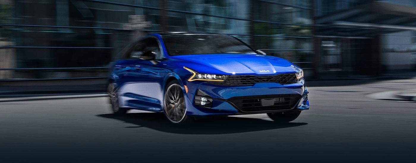 A blue 2025 Kia K5 driving in a city