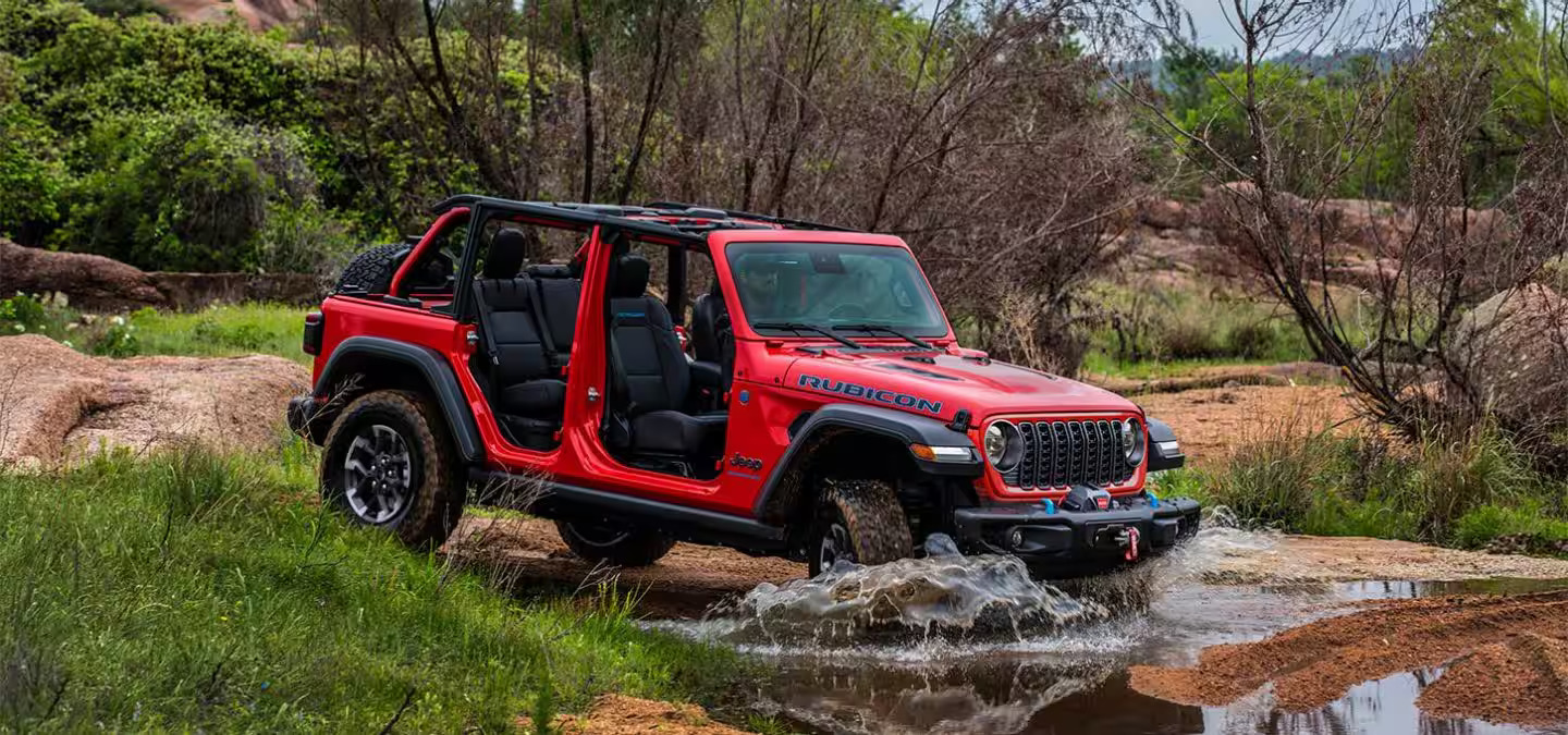 A red jeep driving through some water.