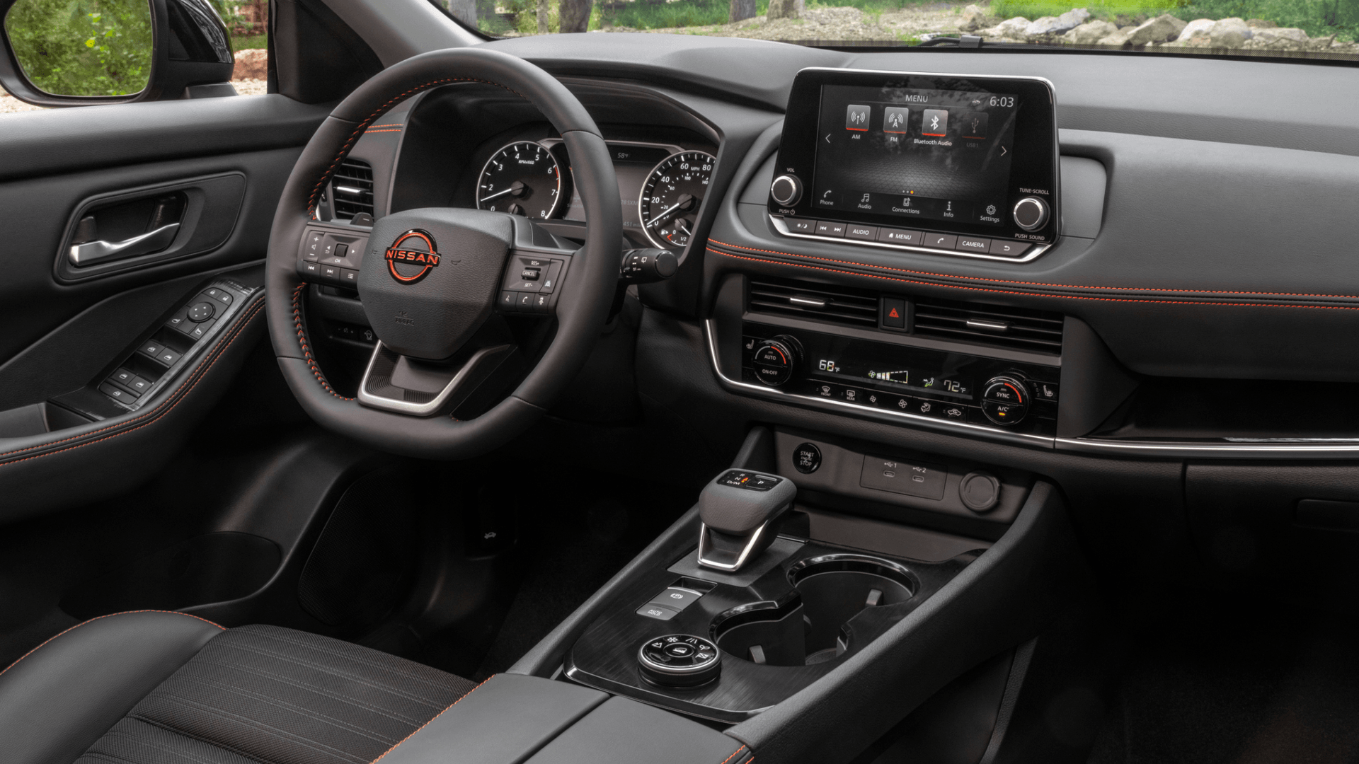 2026 Nissan Rogue® interior showing steering wheel, infotainment screen, center console, and orange stitching.