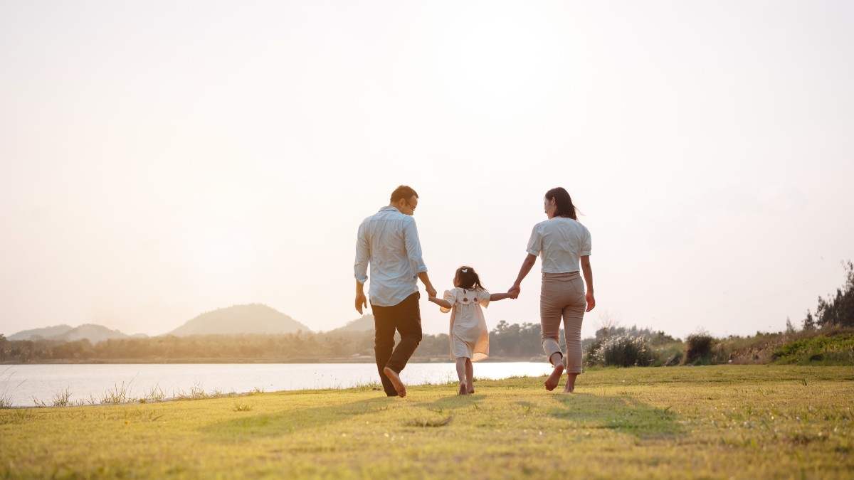 Mother and Father holding Child's Hands Between Them Walking through Field Away from Camera