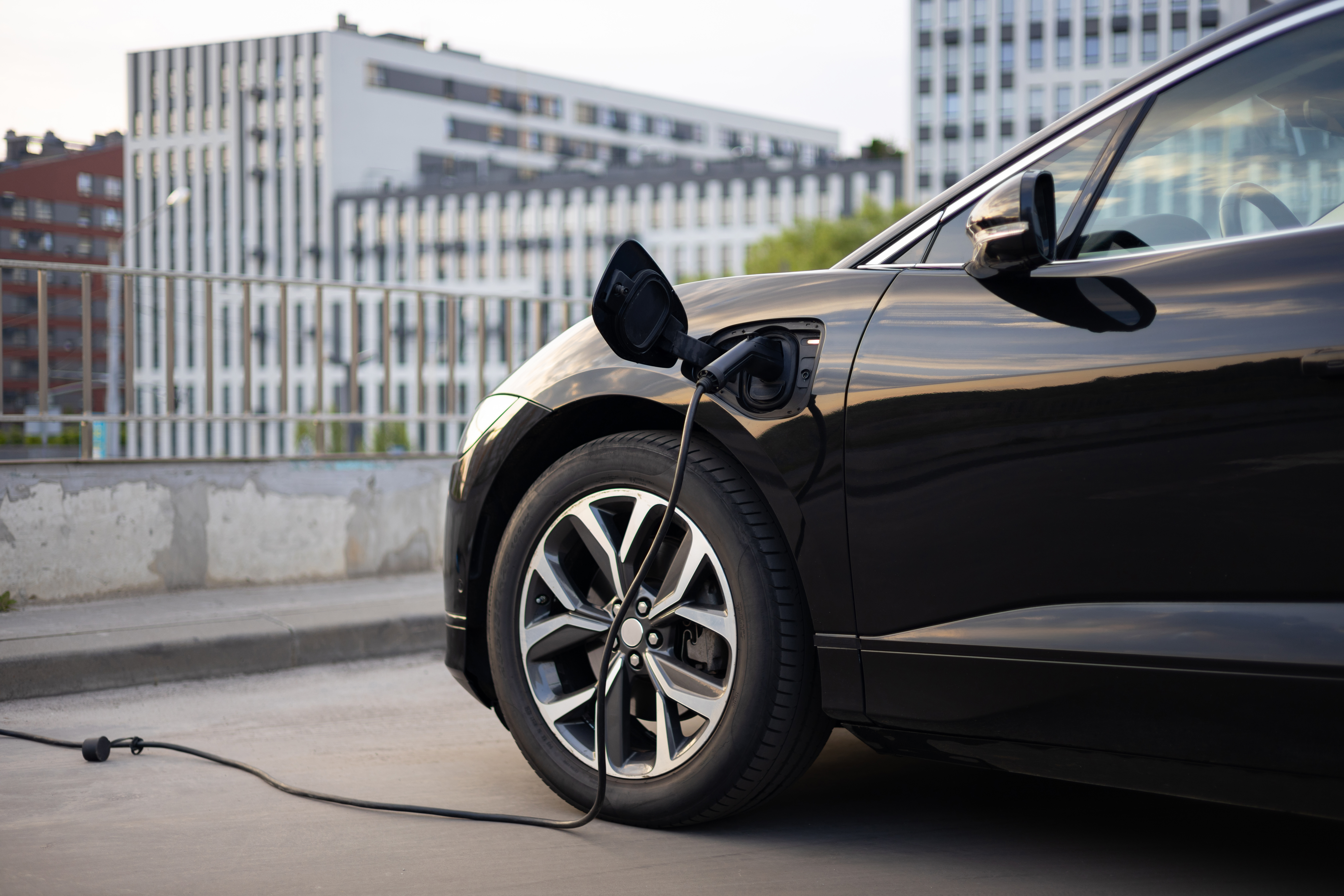 Close-up of a modern NACS EV fast-charging cable plugged into a clean white vehicle at a public charging station."