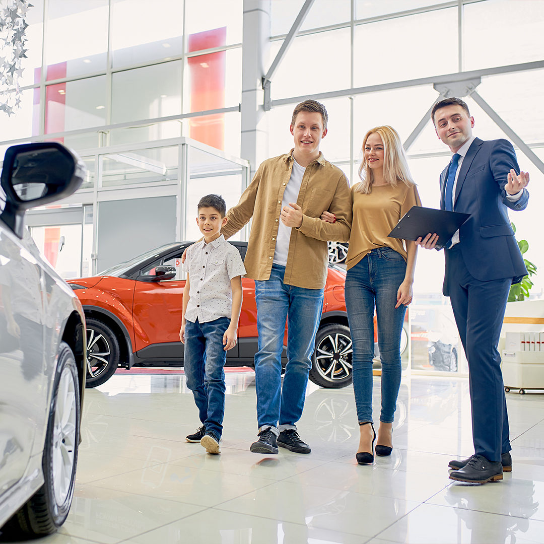 Family speaks with salesman in car dealership showroom