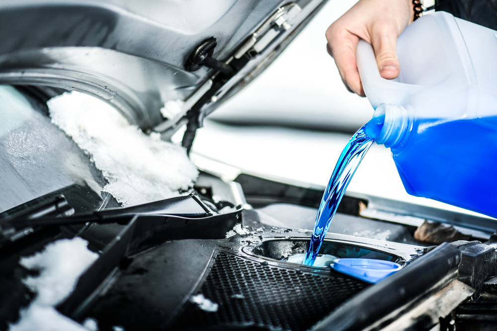 Person pouring blue coolant into a car's engine.