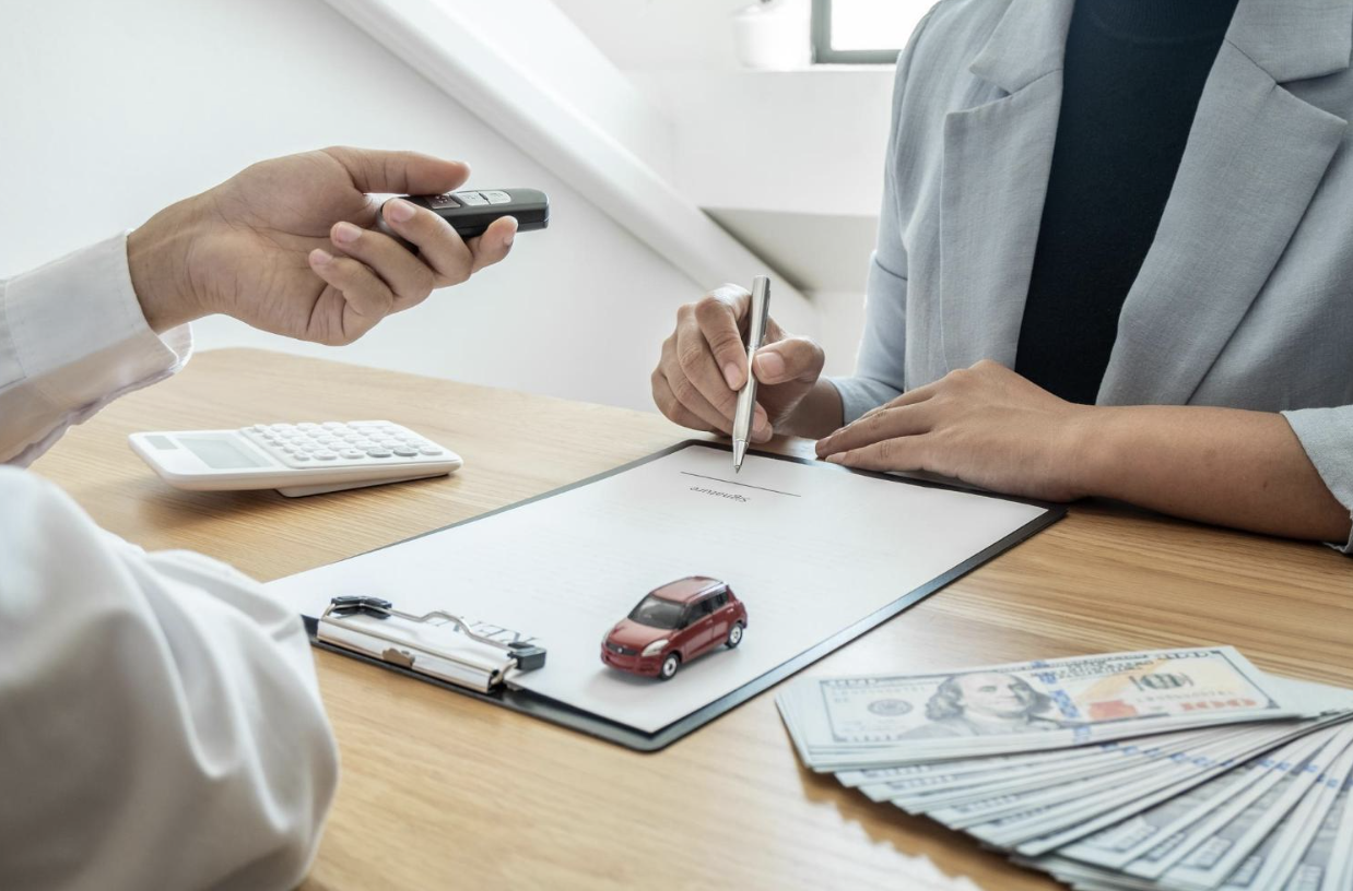Car buyer signing a contract while receiving keys with money on the table.