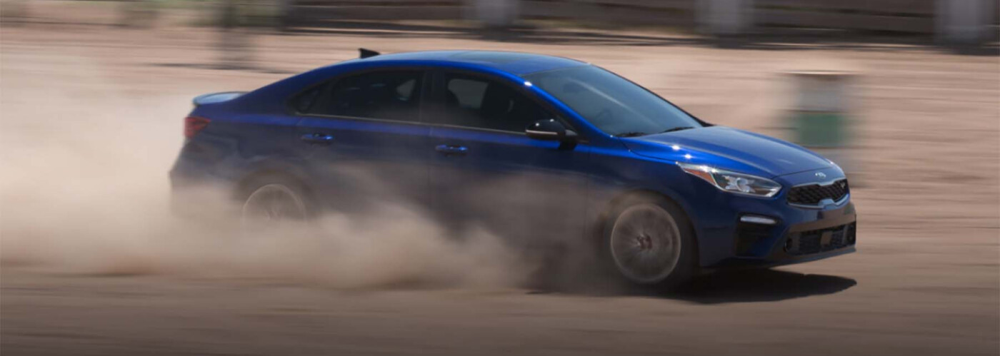 Blue Kia sedan drifting on dirt track, showcasing performance and handling, relevant to used car mileage considerations at Kiefer Kia.